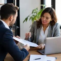 Doradca omawia z klientem ofertę ubezpieczenia chorobowego B2B, analizując dokumenty przy laptopie.