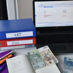 Segregator VAT i ZUS, laptop z arkuszem kalkulacyjnym, pieniądze i notatnik. To obrazuje, co to znaczy być vatowcem na ryczałcie.