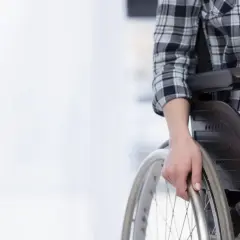 Osoba na wózku inwalidzkim, z orzeczeniem umiarkowanym, przygotowuje się do pracy. Dłoń spoczywa na obręczy koła.