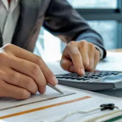 Biznesmen liczy koszty, planując najem powyżej 100 tys. zł. Analiza dokumentów i kalkulacja na biurku.