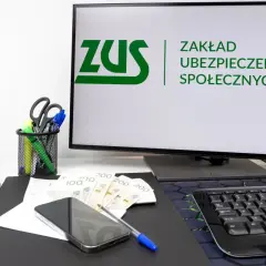 Biurko z komputerem wyświetlającym logo ZUS, pieniędzmi i telefonem. Rozważasz wynagrodzenie członka zarządu a ZUS?