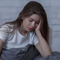 Smutna dziewczyna w łóżku, oparta głową o dłoń. Czeka na l4 od psychiatry, czując się przygnębiona.