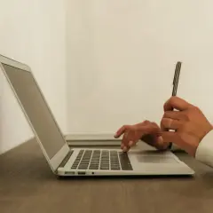 Ręce piszą na laptopie, szukając informacji, jak przejść na b2b. Długopis w dłoni sugeruje planowanie.