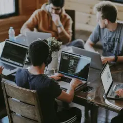 Grupa młodych ludzi pracuje przy laptopach, dyskutując o tym, w jakim wieku można założyć firmę.