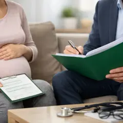 Kobieta w zaawansowanej ciąży, l4 w ciąży, rozmawia z lekarzem, który notuje informacje.