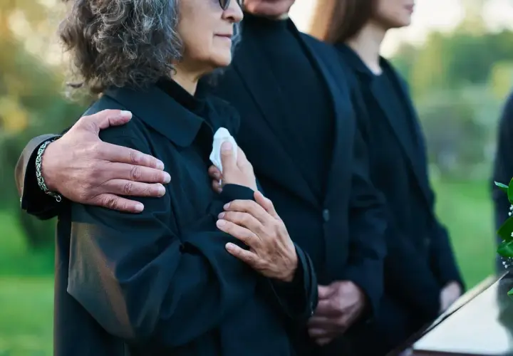 Odprawa pośmiertna: bliscy w żałobie, objęci ramieniem, trzymają chusteczkę.