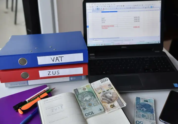 Segregator VAT i ZUS, laptop z arkuszem kalkulacyjnym, pieniądze i notatnik. To obrazuje, co to znaczy być vatowcem na ryczałcie.