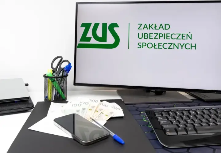 Biurko z komputerem wyświetlającym logo ZUS, pieniędzmi i telefonem. Rozważasz wynagrodzenie członka zarządu a ZUS?
