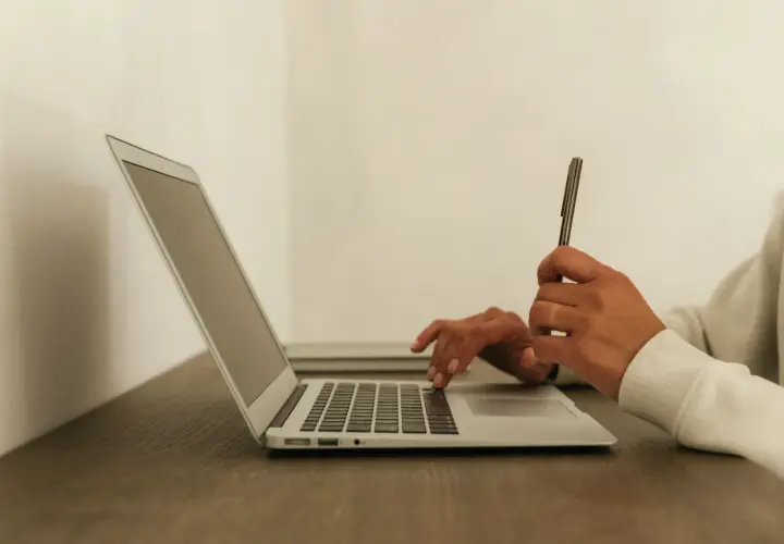 Ręce piszą na laptopie, szukając informacji, jak przejść na b2b. Długopis w dłoni sugeruje planowanie.