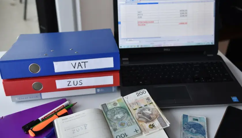 Segregator VAT i ZUS, laptop z arkuszem kalkulacyjnym, pieniądze i notatnik. To obrazuje, co to znaczy być vatowcem na ryczałcie.