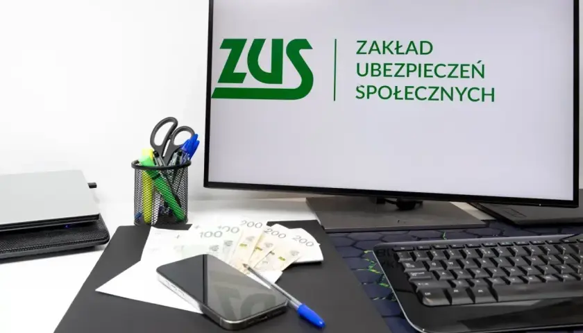 Biurko z monitorem ZUS, telefonem, pieniędzmi i artykułami piśmienniczymi. Idealne miejsce dla osoby współpracującej z urzędem.