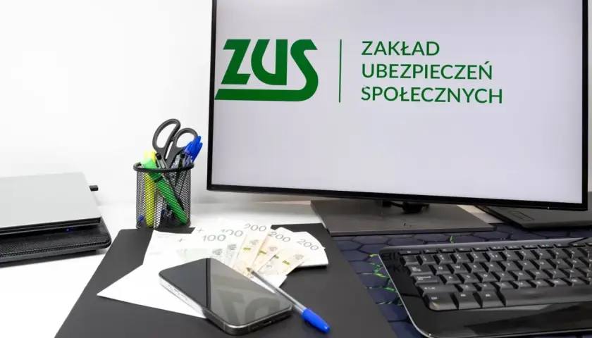 Biurko z komputerem wyświetlającym logo ZUS, pieniędzmi i telefonem. Rozważasz wynagrodzenie członka zarządu a ZUS?