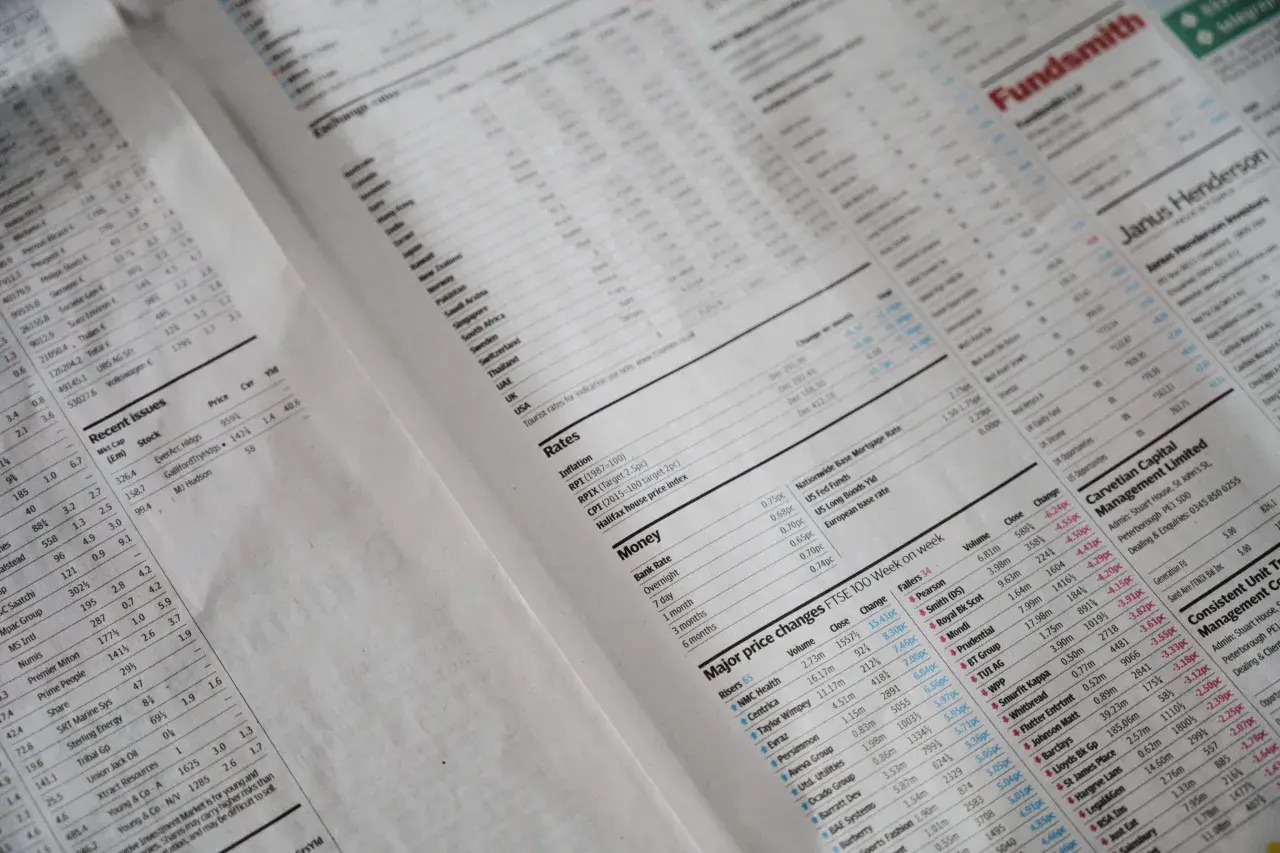 Gazeta finansowa z wykresami i tabelami, zawierająca m.in. ceny akcji i kursy walut. Widać nagłówki takie jak "Rates", "Money", "Major price changes FTSE 100 Week on week", a także przykłady cen transferowych.