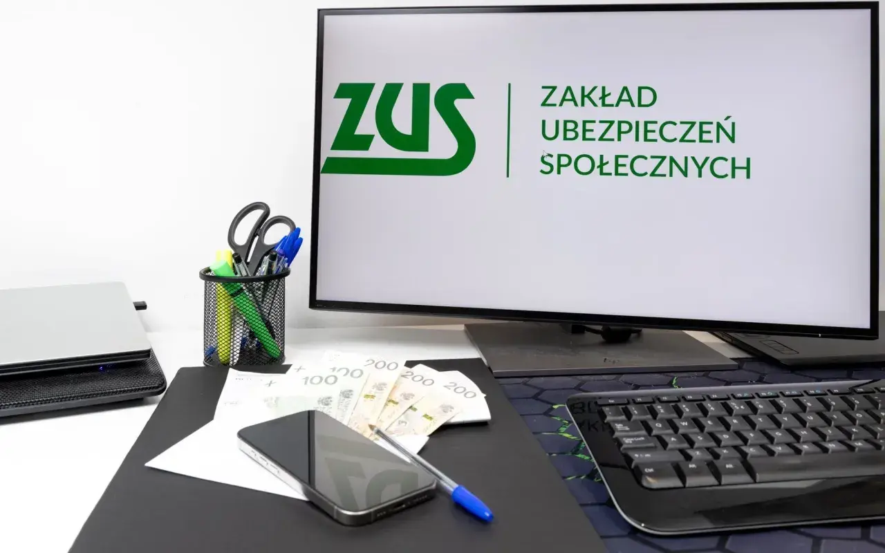 Biurko z komputerem wyświetlającym logo ZUS, pieniędzmi i telefonem. Rozważasz wynagrodzenie członka zarządu a ZUS?